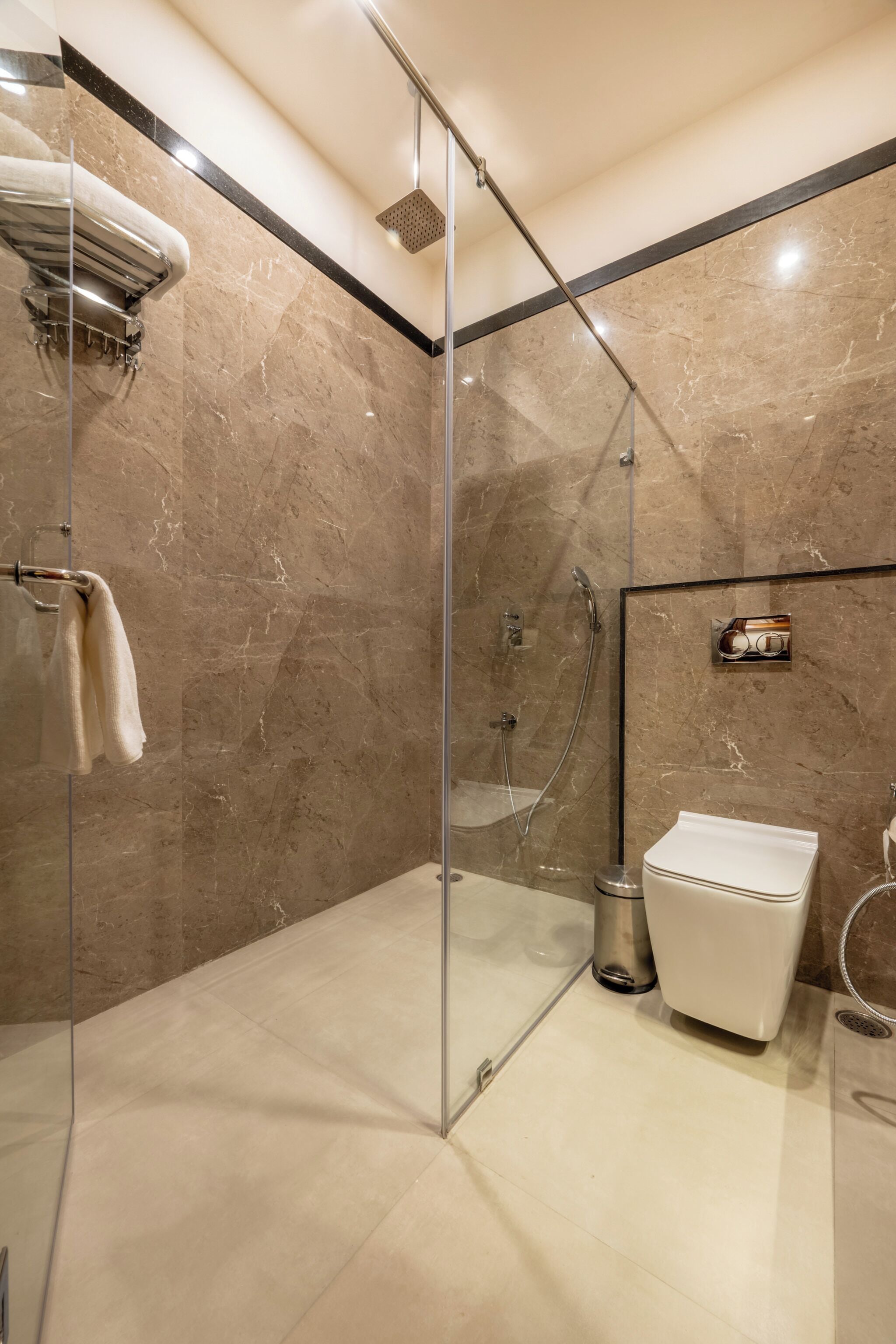 A modern bathroom with a glass-enclosed shower, a white sink, and a marble-tiled wall.