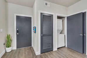 Un couloir avec une porte grise, une porte blanche avec une serrure bleue et une porte blanche dotée d’un ferme-porte gris.