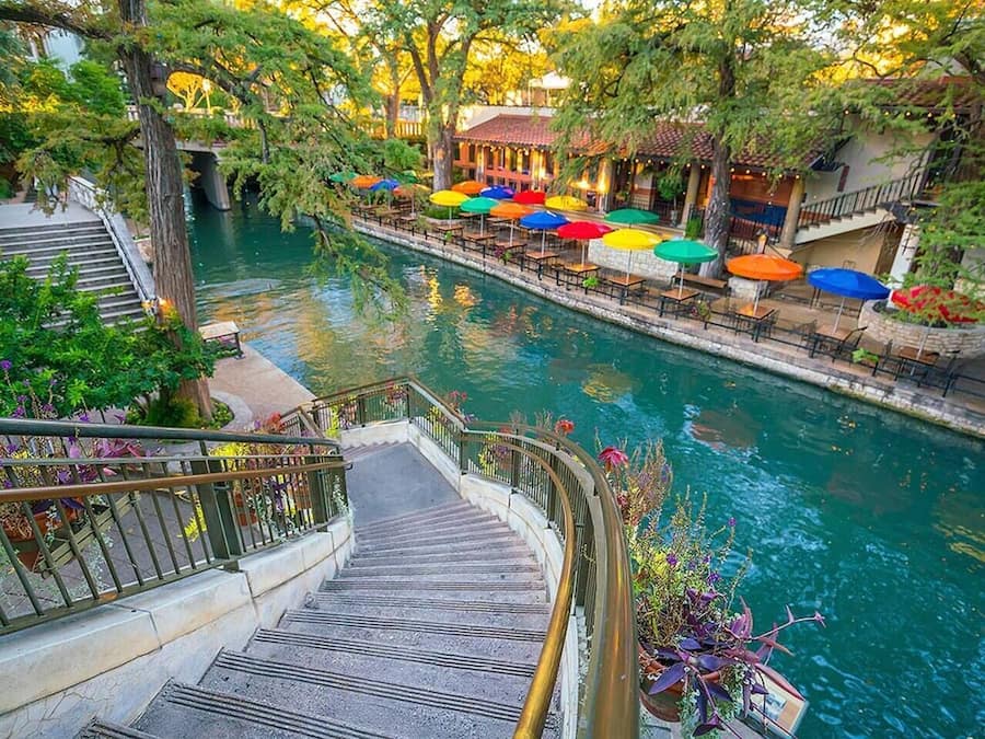 A riverside walkway with outdoor seating and a staircase leading down to the water.