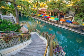 Un paseo a orillas del río con mesas al aire libre y una escalera que baja hacia el agua.