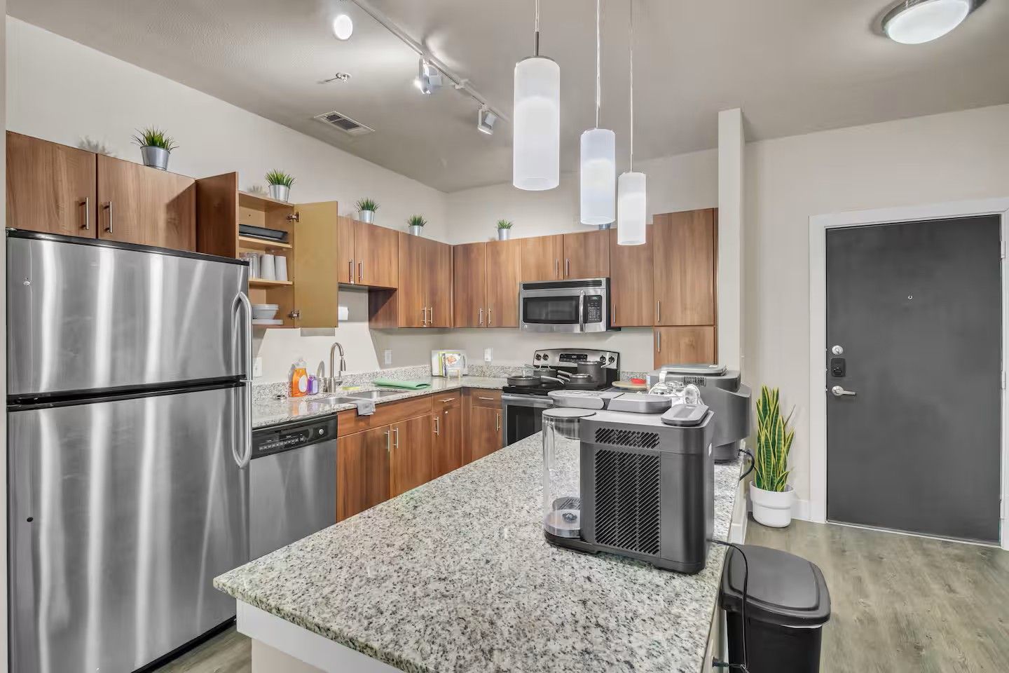 A modern kitchen with stainless steel appliances, wooden cabinets, granite countertops, and pendant lighting.