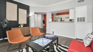 Een moderne woonkamer met twee oranje fauteuils, een zwarte salontafel met een spel, een rode bank en een keuken op de achtergrond.