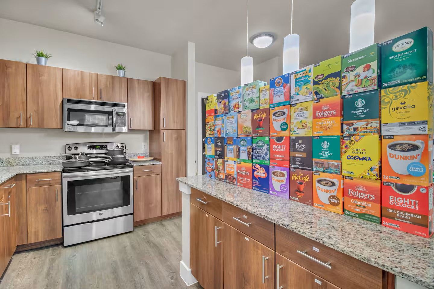 A kitchen with wooden cabinets, a microwave, stove, and a countertop displaying various coffee and tea boxes.