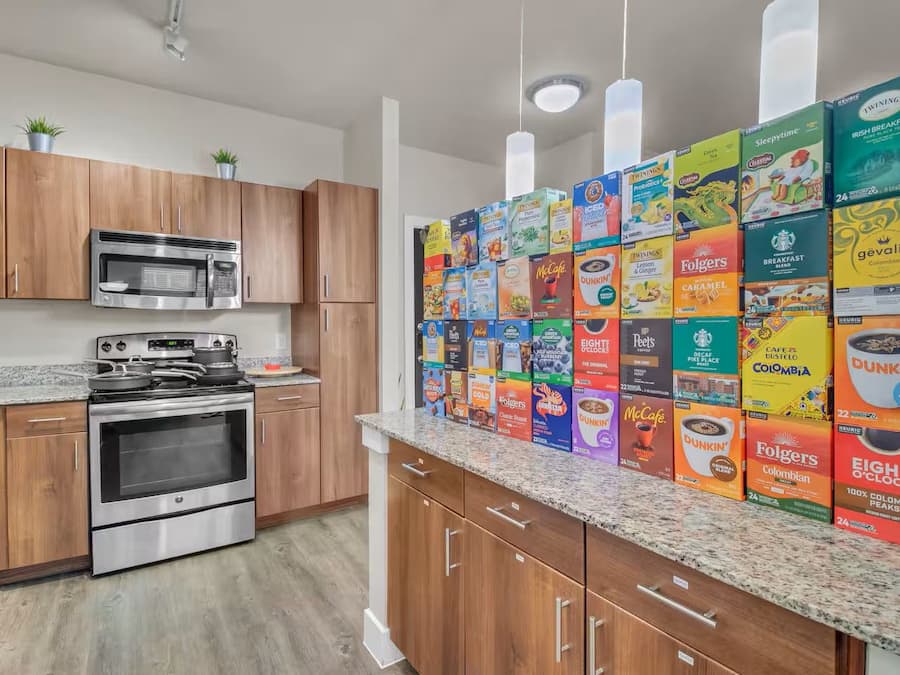 A kitchen with wooden cabinets, a microwave, stove, and a countertop displaying various coffee and tea boxes.