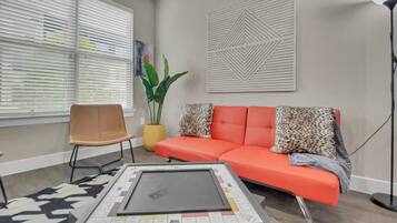 Ein Wohnzimmer mit einer Couch, einem Sessel, einem Couchtisch, einer Pflanze und einem Wandbild.