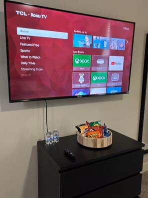 Un téléviseur fixé au mur affiche l’interface Roku TV, avec différents choix de menu.