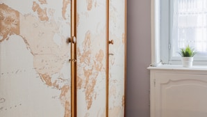 A white wardrobe with a world map design, a window with a plant, and a white cabinet. - Studio Gar by Wonderful Italy (Turin)