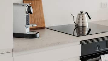 Eine moderne Küche mit integrierter Espressomaschine, einem Holzer Schneidebrett und einem Wasserkocher auf einer Glasarbeitsplatte.