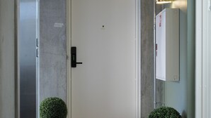 A hallway with a white door, two potted plants, a doormat, and a thermostat on the wall. - Clover House by Daniel&Jacob's (Copenhagen)