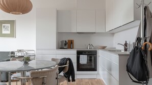 A modern kitchen with white cabinets, a round dining table, and chairs. There is a coffee machine, an oven, and a hanging coat rack. - Clover House by Daniel&Jacob's (Copenhagen)