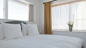 A neatly made bed with white linens, a window with beige curtains, and a vase with flowers on the windowsill. - Clover House by Daniel&Jacob's (Copenhagen)