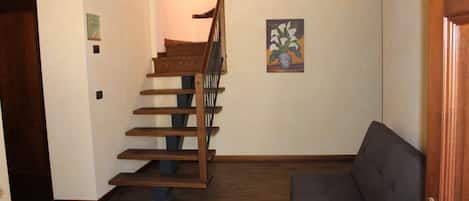 Una escalera de madera con barandilla, un sofá gris y un cuadro de flores en la pared.