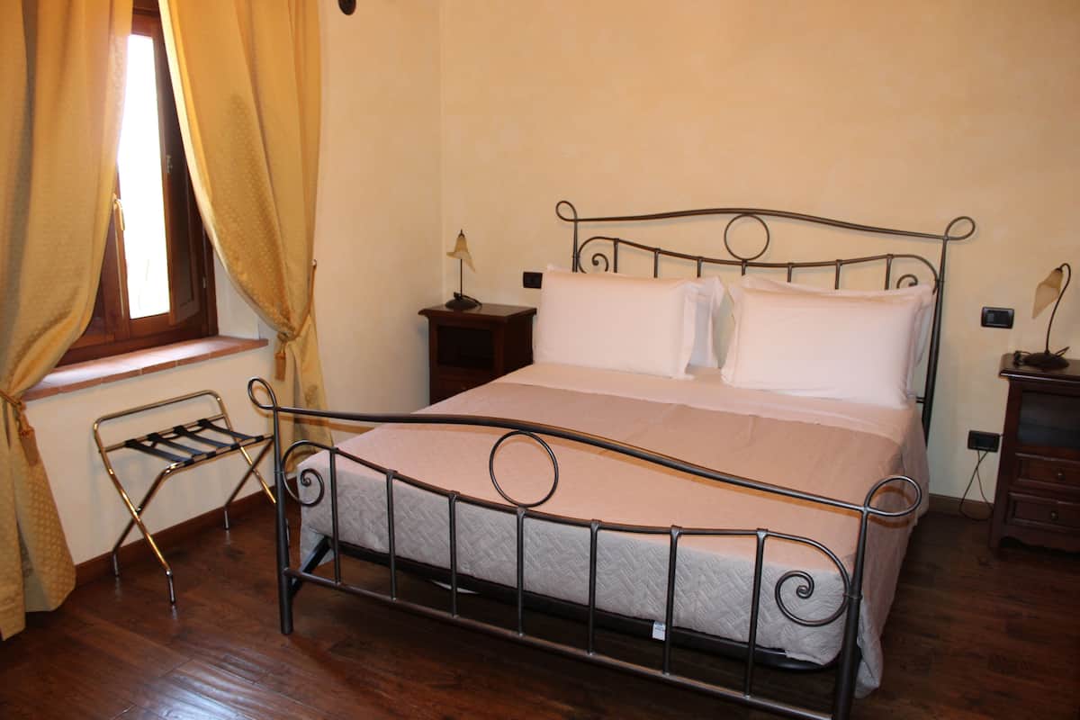 Una cama individual con estructura metálica, una mesita de noche de madera con lámpara y una ventana con cortinas.
