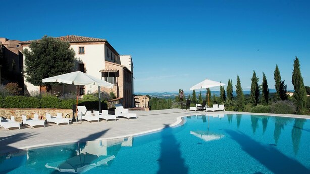A swimming pool with lounge chairs and umbrellas, surrounded by buildings and trees. - Nuovo Etruria Resort (Montepulciano)