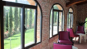 A room with large arched windows, brick walls, and wooden beams. There are two purple chairs and a small table. - Nuovo Etruria Resort (Montepulciano)