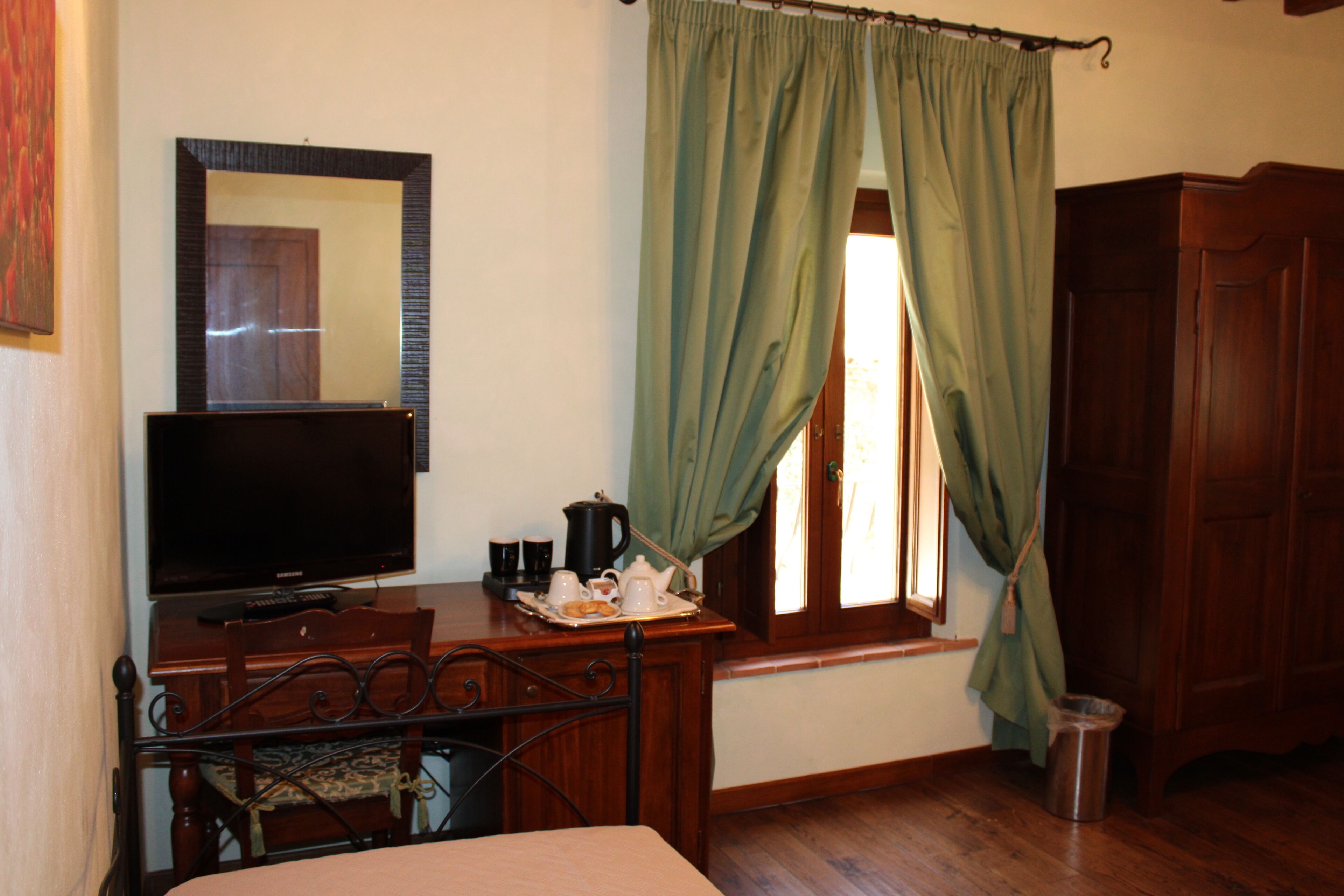 Une chambre à coucher avec un lit, un téléviseur posé sur une commode en bois, une fenêtre avec des rideaux verts et une armoire en bois.