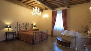 Un dormitorio con techo de madera, cama con estructura metálica, candelabro, mesita de noche, lámpara, ventana con cortinas y baño con bañera.