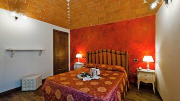A hotel room with a wooden headboard, a bed with floral bedding, two bedside tables with lamps, a small white bedside table, and a wooden floor.