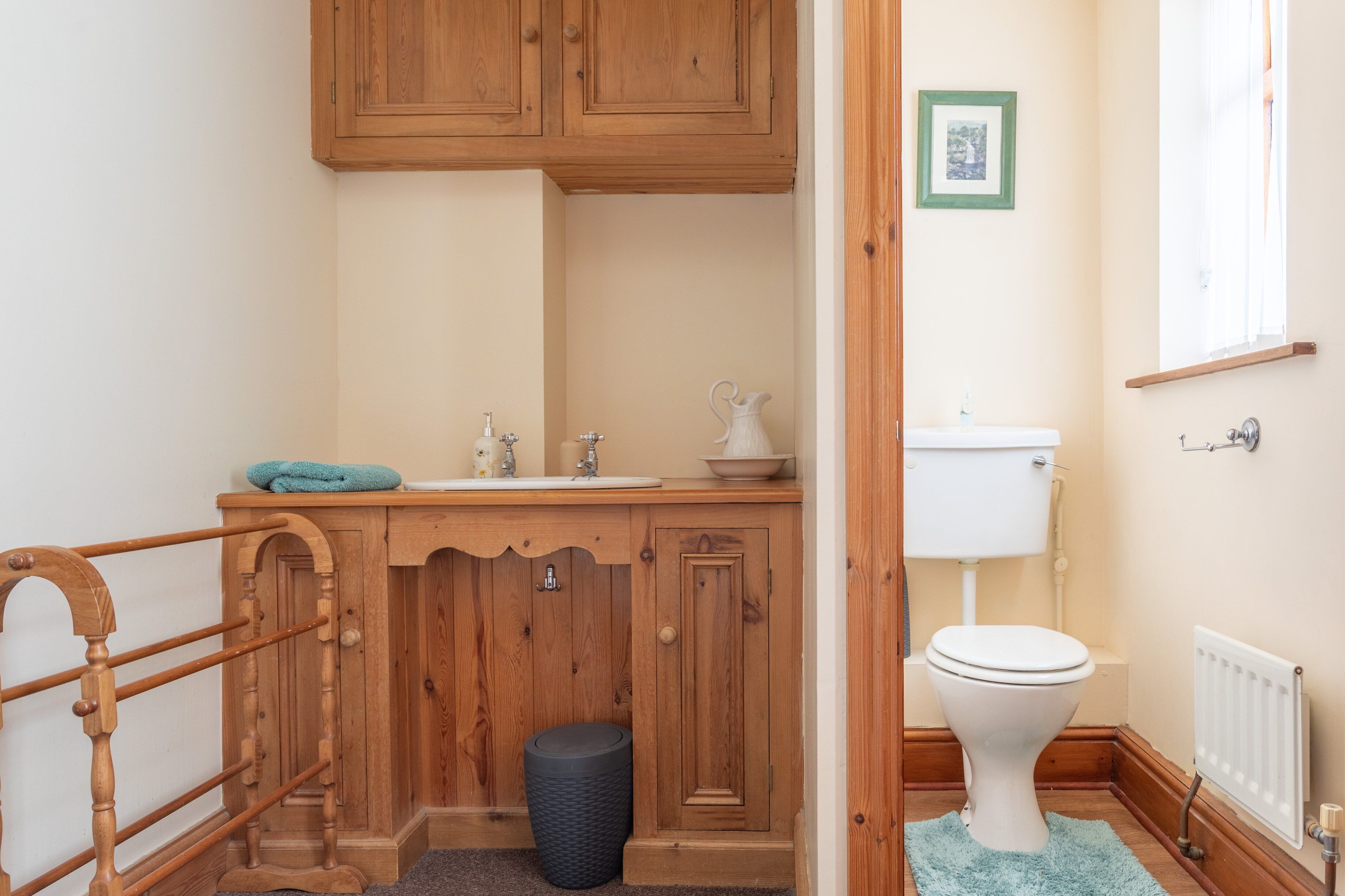 A bathroom with wooden cabinets, a white sink, a toilet, and a black waste bin.
