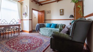 Ein Wohnzimmer mit Holzboden, einem grünen Sofa, einem gemusterten Teppich und einem Essbereich mit Tisch und Stühlen.