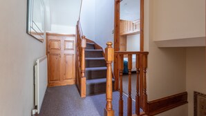 Eine Treppe mit hölzernen Geländern und Teppichstufen führt zu einer Zwischenebene mit einer Holztür und einem Heizkörper.