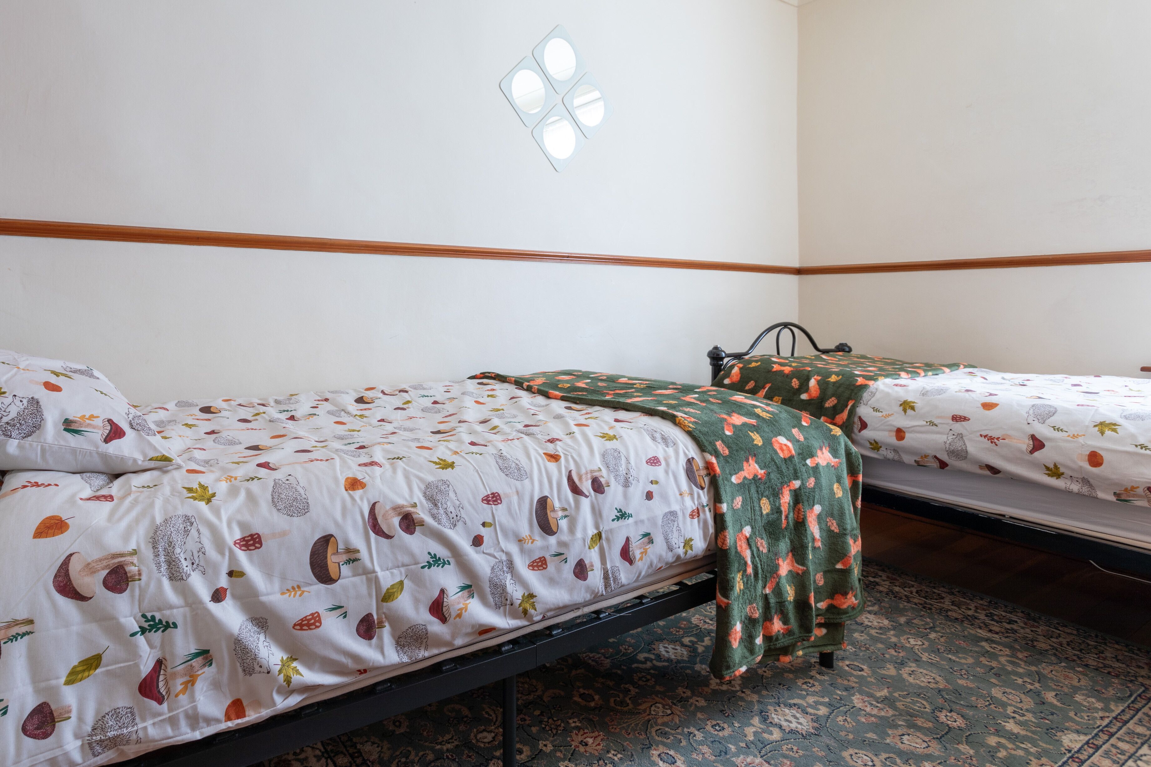 Una habitación con dos camas individuales, cada una con ropa de cama estampada y una manta verde.