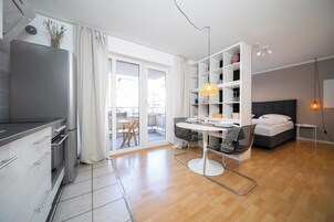 A modern, well-lit room with a kitchenette, a dining area, and a bedroom.