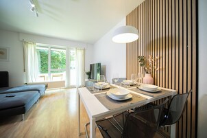 A modern dining area with a table set for four, a sofa in the background, and a view of greenery outside.