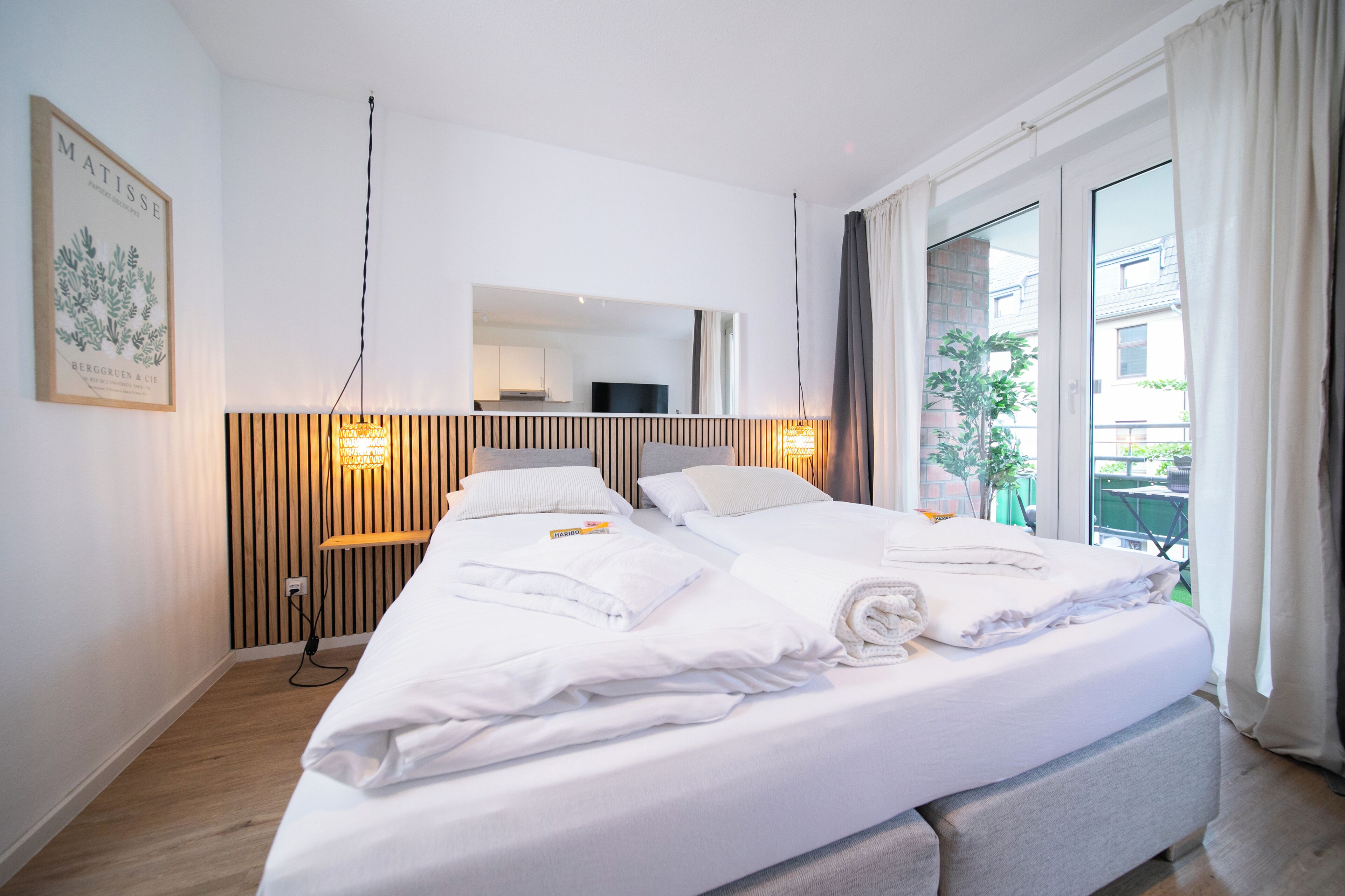 Ein modernes Hotelzimmer mit einem großen Bett, einem hölzernen Kopfteil, einem Flachbildfernseher und einem Balkon mit Blick ins Freie.
