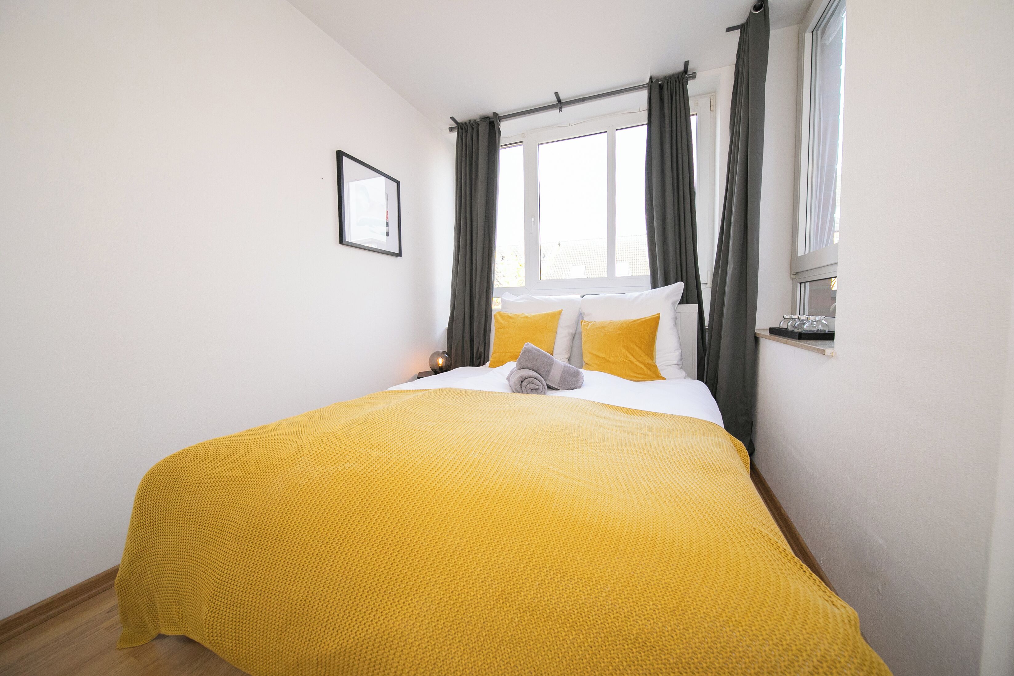 Un lit bien fait, avec une couverture jaune, un oreiller blanc et une serviette grise.