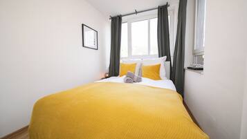 Un lit bien fait, avec une couverture jaune, un oreiller blanc et une serviette grise.