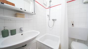 Ein Badezimmer mit einem weißen Waschbecken, einer Badewanne und einer Toilette. Auf dem Waschbecken stehen zwei grüne Flaschen.