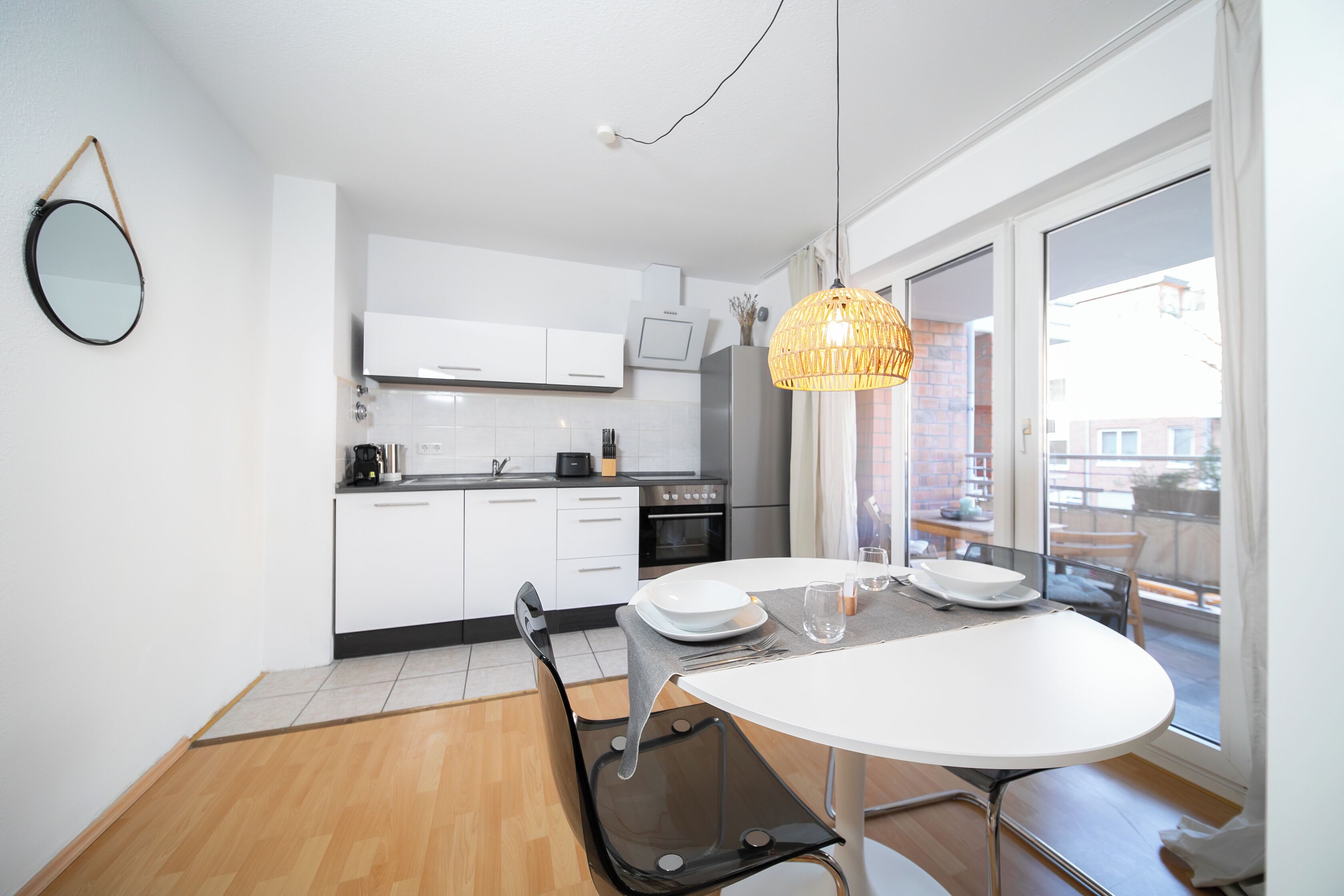 A modern kitchen with white cabinets, a dining table with chairs, and a large window with a view of the city.