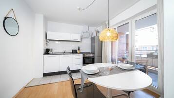 A modern kitchen with white cabinets, a dining table with chairs, and a large window with a view of the city.