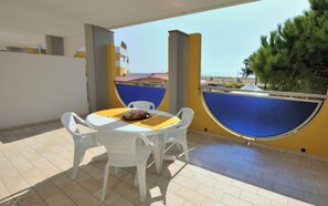 A patio with a round table and four chairs, a blue and yellow wall, and a view of buildings and trees.