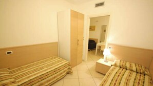 A hotel room with two single beds, a bedside table with a lamp, and a door leading to another room. - Family Holiday Flat With Pool for six (San Michele al Tagliamento)
