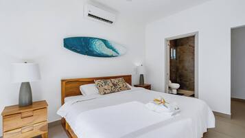 A bedroom with a bed, a nightstand, a wall-mounted air conditioner, a ceiling fan, and a bathroom door.