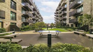 Un moderno edificio de apartamentos con balcones, un patio con mesa de tenis y zonas verdes circundantes.