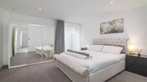 Un dormitorio moderno con una cama grande, un espejo, una mesita de noche con lámpara y un cuadro en la pared.