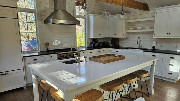 A modern kitchen with a large island, white cabinetry, and wooden bar stools. - Coastal home in Brewster near beaches and bike path RPMS161 (Brewtser)