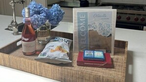 A kitchen counter with a welcome sign, a bottle of wine, a basket of bread, and a box of chocolate. - Coastal home in Brewster near beaches and bike path RPMS161 (Brewtser)