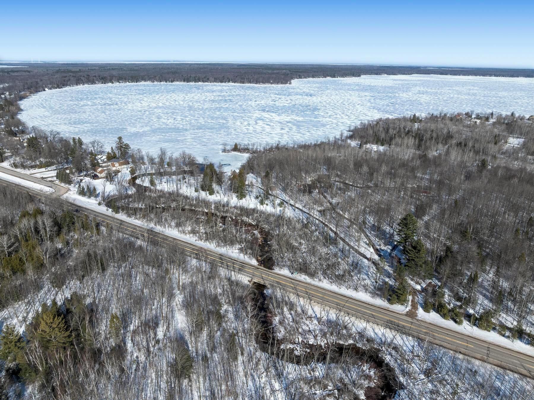 Un paysage hivernal avec un lac gelé, une autoroute et une forêt clairsemée.