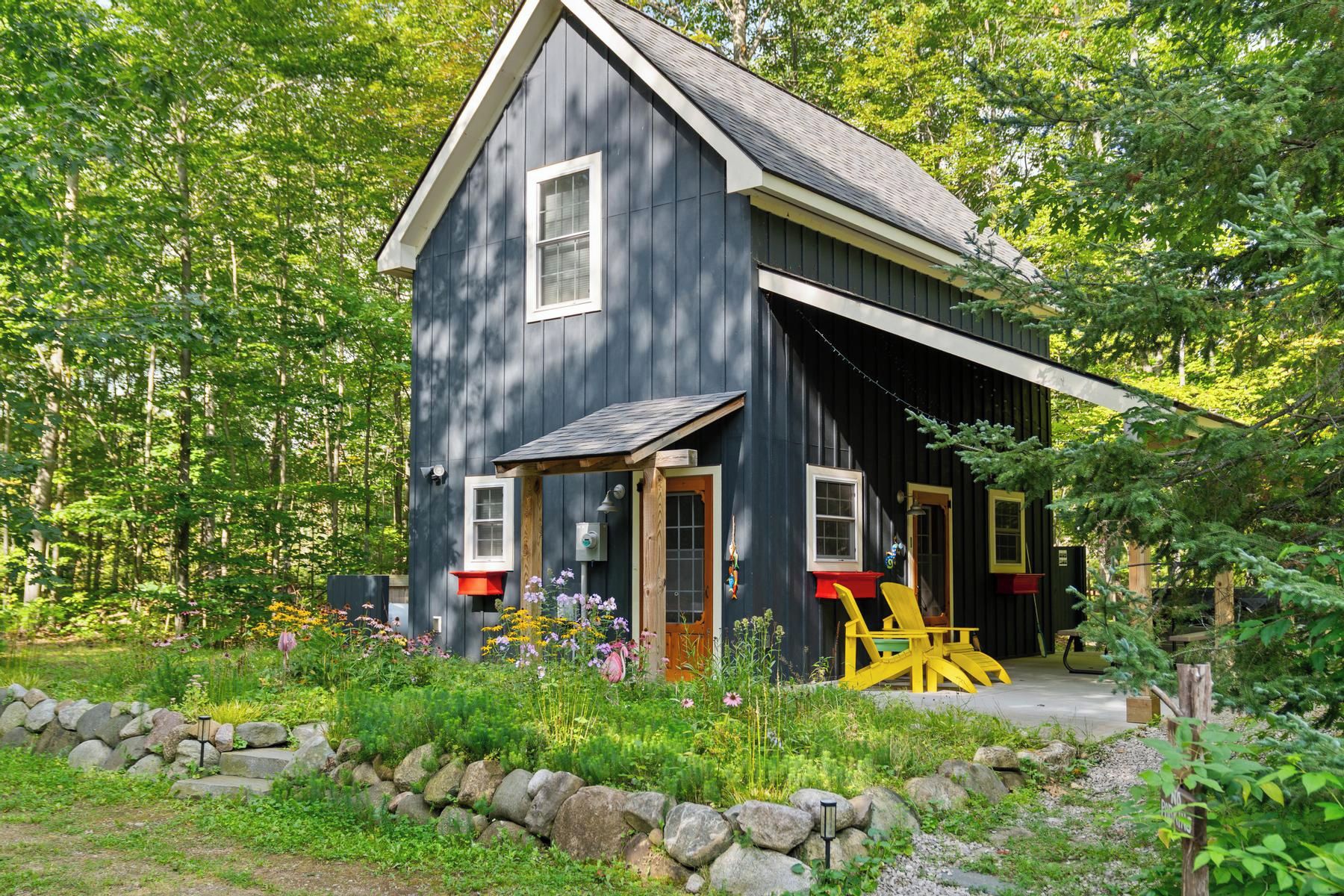 A rustic cabin with a large porch, surrounded by a garden and a stone wall.