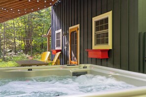 Ett område med ett bubbelbadkar, två stolar, ett trädäck och ett hus med en myggnätsdörr och myggnätsfönster.