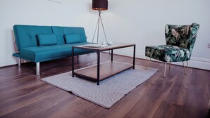A living room with a teal sofa, a wooden coffee table, a floor lamp, and a patterned armchair. - Converted bank: centre of Town (split apartment) (Holmfirth)