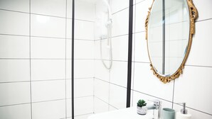 A bathroom with white tiled walls, a white sink, a gold-framed mirror, and a shower. - Converted bank: centre of Town (split apartment) (Holmfirth)