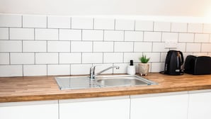 A kitchen with a wooden countertop, white cabinets, a sink, a kettle, and a small plant. - Converted bank: centre of Town (split apartment) (Holmfirth)
