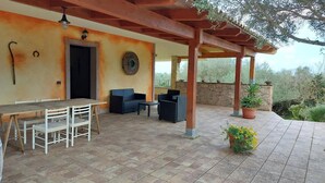 A covered patio area with a table and chairs, a stone wall, and potted plants. - Sardinia Re - Country Villa Pala Venalza Loft (Olmedo)