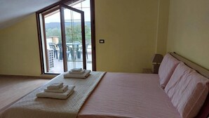 A bedroom with a large bed, a balcony with chairs, and a view of greenery. - Sardinia Re - Country Villa Pala Venalza Mansarda (Olmedo)