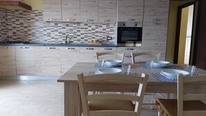 A modern kitchen with a tiled backsplash, a built-in oven, and a dining area with a table set for four. - Sardinia Re - Country Villa Pala Venalza Mansarda (Olmedo)